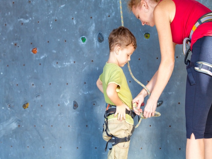 A instructor checking the safety harness of the boy before climbing, 