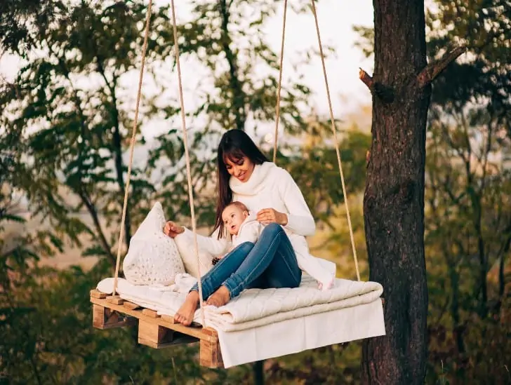 A mother and a baby on a swing bed outdoors.