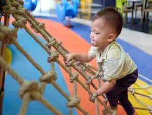 A toddler climbing on the rope net.
