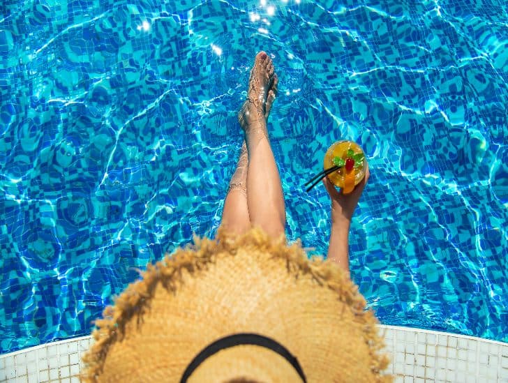 A top view of a woman drinking cocktail beside the pool. 