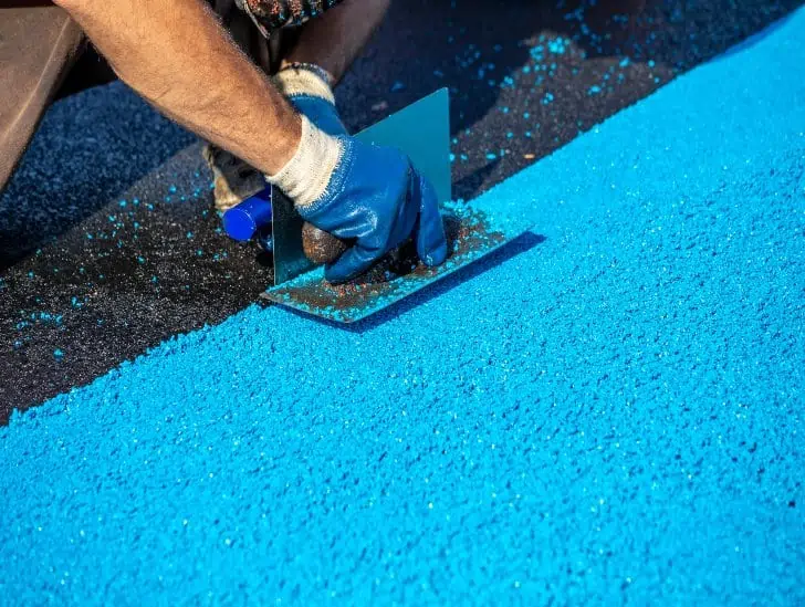 A worker installing rubber mulch on playgrounds surface. 